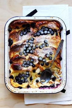 a casserole dish with blueberries and powdered sugar on the side, next to a spoon