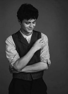 black and white photograph of a man wearing a vest with his arms crossed looking down