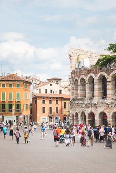 many people are walking around in an old town square with ancient buildings and stone arches