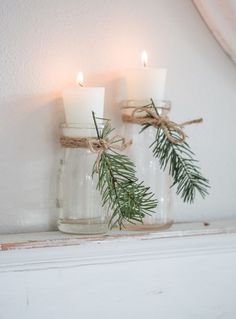 three candles are placed in glass jars with twine and pine needles tied to them