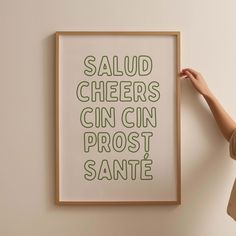 a person holding up a framed poster with the words, salud cheers gin gin post sante