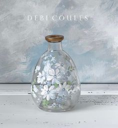 a glass vase with white flowers painted on it and the words debi coulees above it