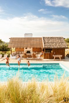 three people jumping into a swimming pool in front of a wooden structure with a thatched roof