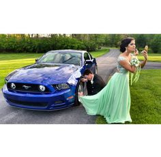 a woman in a green dress standing next to a blue mustang