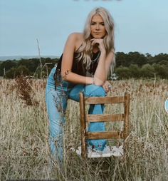 a woman sitting on top of a wooden chair in a field