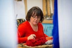 a woman is weaving red yarn on a table