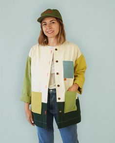 a woman standing in front of a blue wall wearing a green hat and colorful jacket