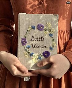 a woman holding a book with the words little women written on it in front of her