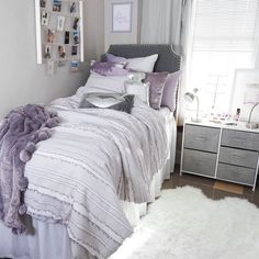 a bed with purple and white comforters in a bedroom next to a window filled with pictures