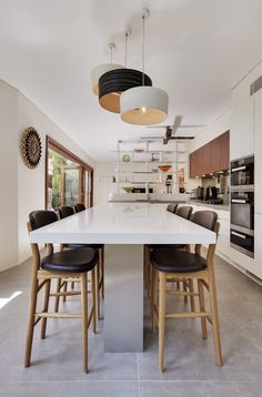 a large kitchen with an island table surrounded by stools and lights hanging from the ceiling