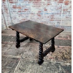 an old wooden table sitting in front of a brick wall with black legs on it