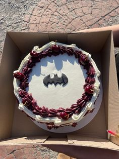 a cake in a box with a batman symbol on it's top and red berries around the edges