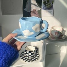 a person holding a cup and saucer in front of a shelf with other items on it