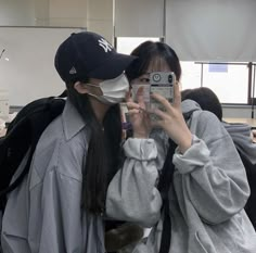 two people wearing face masks taking pictures with their cell phones in front of them at an airport