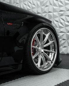 a black sports car with chrome rims parked in front of a white and gray wall