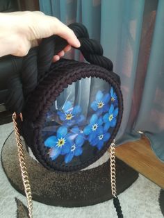 a hand holding a purse with blue flowers on the front and side, while it is being held by someone's hand