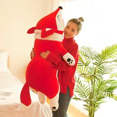 a woman in a red sweater holding a large stuffed animal that looks like a fox