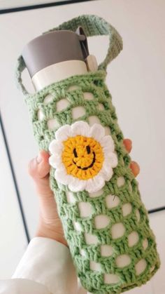 a person holding up a green crocheted water bottle with a smiley face on it