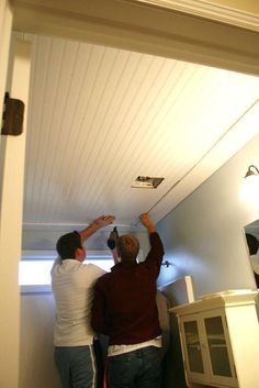 two men are painting the ceiling in their home with white paint and wood trimmings