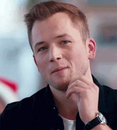 a man sitting down with his hand on his chin and looking at the camera while wearing a watch