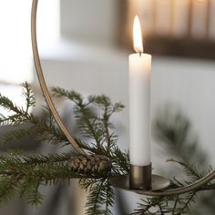 a white candle is lit on a metal holder with pine cones and evergreen branches in the foreground