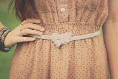 a woman is wearing a dress with a knot on it's belt and has her hands in her pockets