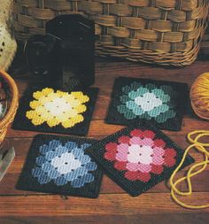 four crocheted coasters sitting on a table next to a basket and yarn