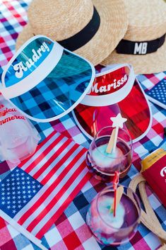 two straw hats sitting on top of a checkered table cloth with drinks and american flags