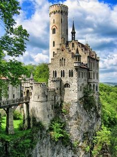 an old castle sitting on top of a cliff in the middle of a lush green forest