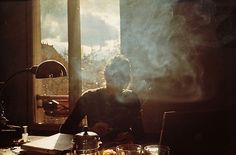 a man sitting in front of a laptop computer on top of a desk next to a window