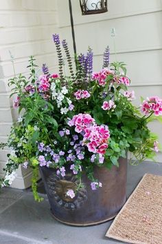 a metal bucket filled with lots of flowers on top of a door mat next to a house