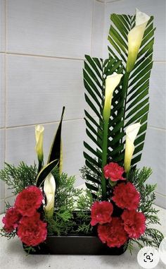 red and white flowers are in a black vase with greenery on the counter top