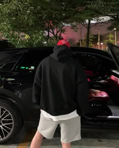 a man in black hoodie and white shorts standing next to a car