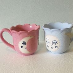 two ceramic mugs sitting on top of a white table next to each other with eyes drawn on them