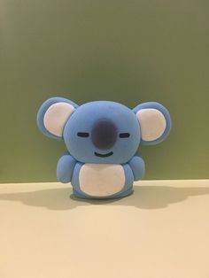 a small blue koala toy sitting on top of a table next to a green wall