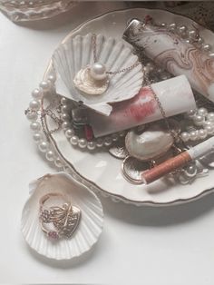 an assortment of jewelry on a plate with pearls and seashells in the background