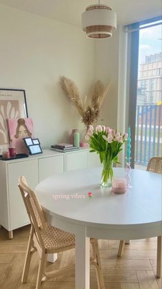 a white table with some flowers on top of it and a vase filled with pink tulips