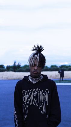 a young man with dreadlocks standing in the middle of a parking lot wearing a black hoodie