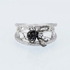 a silver ring with black and white stones on it's sides, in the shape of a spider