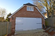 a brick house with a white garage door and window on the top floor, next to a wooden fence