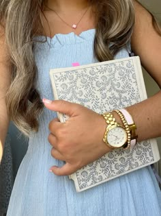 a woman in a blue dress holding a watch and a book on her left hand