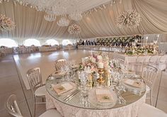 a table set up for a formal dinner in a marquee with chandeliers and white linens