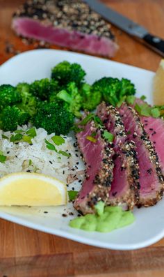 a white plate topped with meat, rice and broccoli next to a lemon wedge