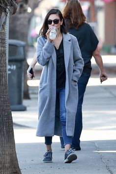 a woman walking down the street while talking on her cell phone and drinking from a cup