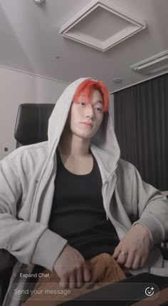 a man with red hair sitting in a chair wearing a hoodie and looking at the camera