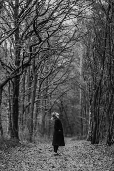 black and white photograph of a woman walking down a path in the woods with bare trees