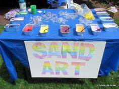 a blue table topped with cupcakes covered in frosting next to a sign that says sand art