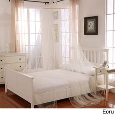 a white bed sitting in a bedroom next to a window with sheer curtains on it