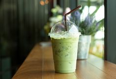 a green smoothie in a plastic cup with a straw sticking out of the top