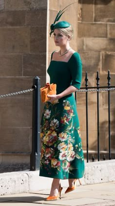 a woman in a green dress and hat is walking down the street with her purse